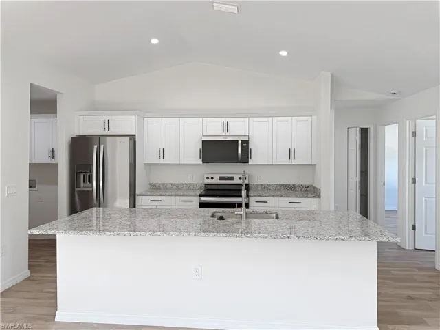 Kitchen featuring light wood-style floors, stainless steel appliances, white cabinetry, light stone countertops, and lofted ceiling