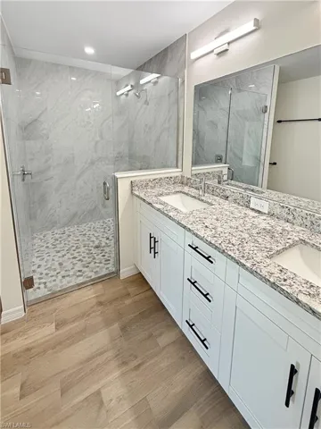 Full bathroom with a marble finish shower, double vanity, and light wood-style flooring