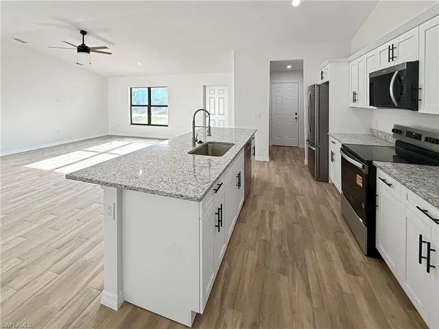 Kitchen featuring stainless steel appliances, white cabinets, light stone counters, a kitchen island with sink, and light wood-style floors