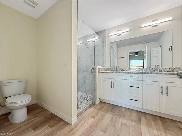 Bathroom with double vanity, a marble finish shower, light wood-type flooring, and ceiling fan