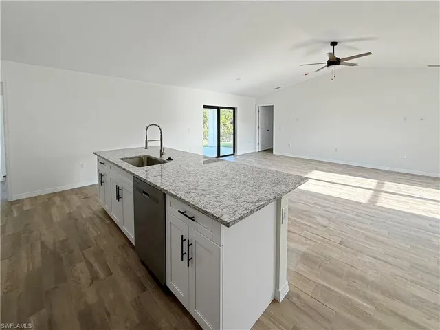Kitchen with white cabinetry, light stone countertops, light wood finished floors, dishwasher, and vaulted ceiling