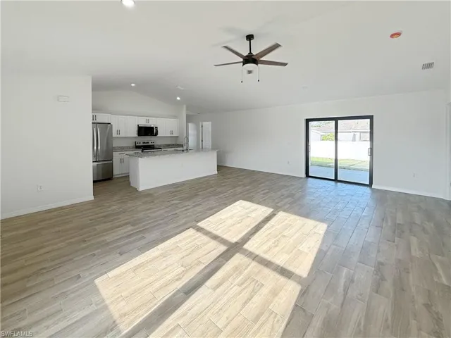 Kitchen featuring lofted ceiling, open floor plan, white cabinetry, stainless steel appliances, and a center island with sink