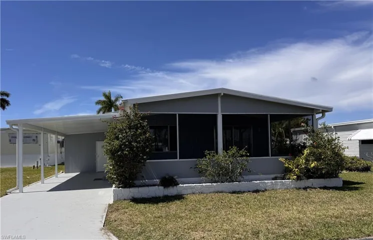 Manufactured / mobile home with a front lawn, an attached carport, driveway, shed, and a sunroom