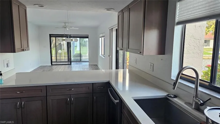 Kitchen featuring stainless steel dishwasher, light countertops, and dark brown cabinets