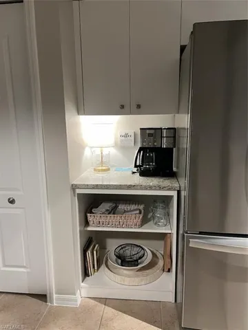 Kitchen with gray cabinetry, light stone countertops, light tile flooring, and fridge