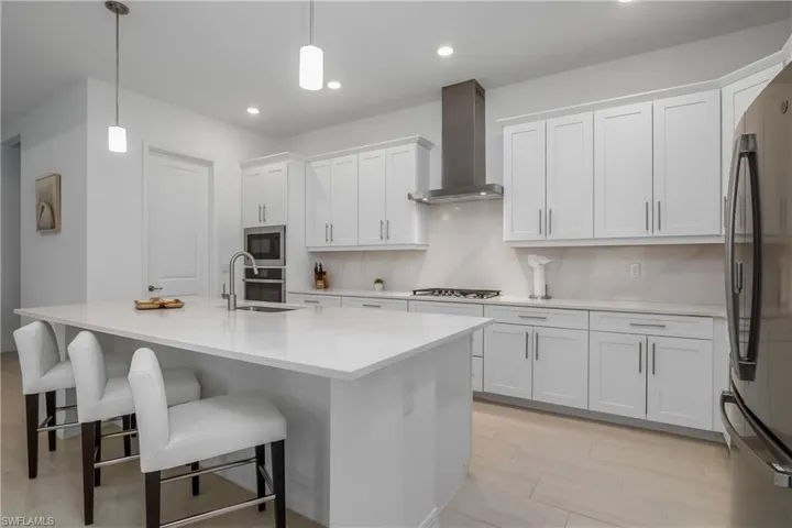 Kitchen featuring a sink, wall chimney range hood, appliances with stainless steel finishes, white cabinets, and recessed lighting
