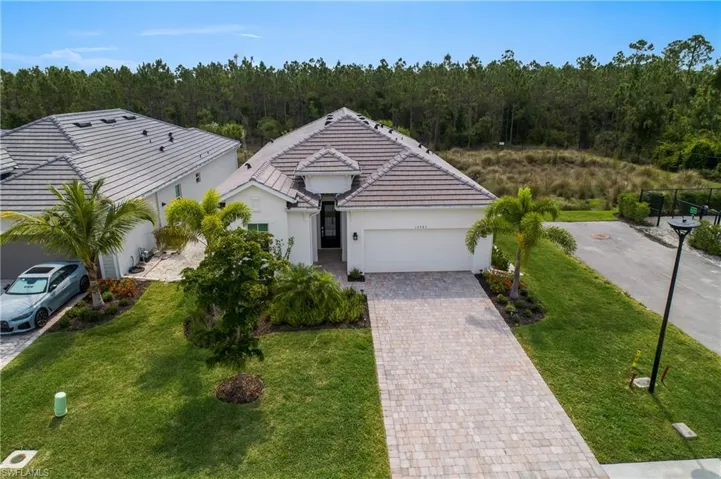 Single story home with a forest view, a garage, decorative driveway, stucco siding, and a front lawn