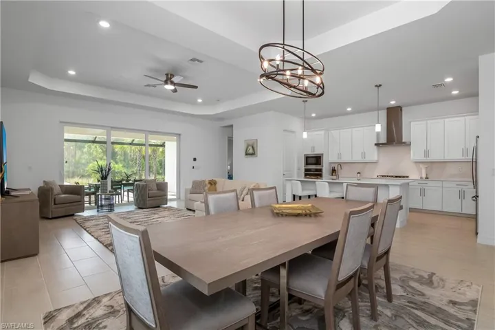 Dining room with a raised ceiling, recessed lighting, a ceiling fan, and a chandelier