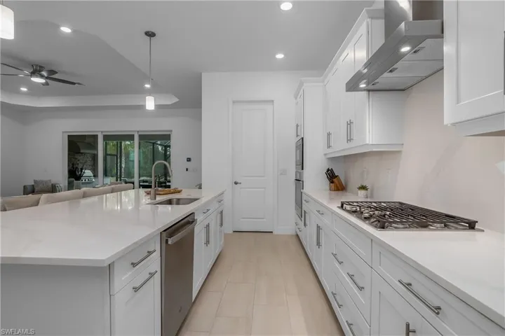 Kitchen with a sink, wall chimney range hood, appliances with stainless steel finishes, recessed lighting, and white cabinetry