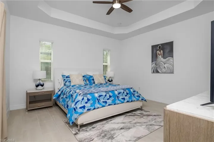 Bedroom with a tray ceiling, multiple windows, baseboards, and ceiling fan