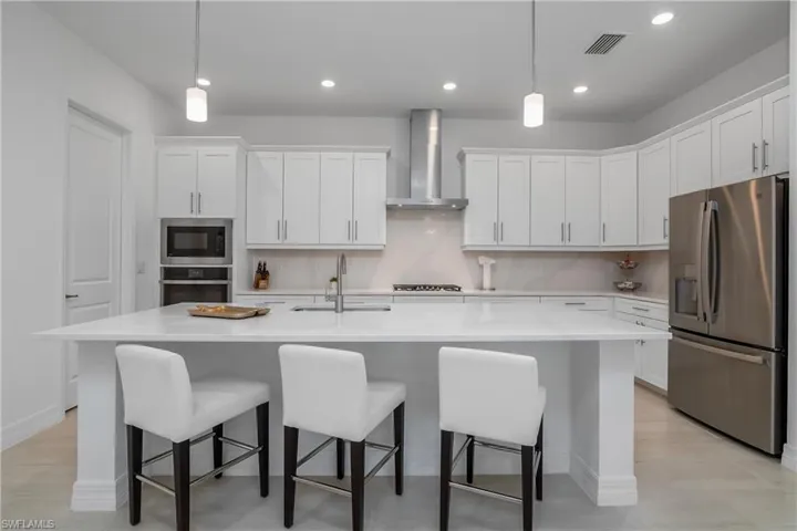 Kitchen featuring stainless steel appliances, wall chimney exhaust hood, a sink, white cabinets, and recessed lighting