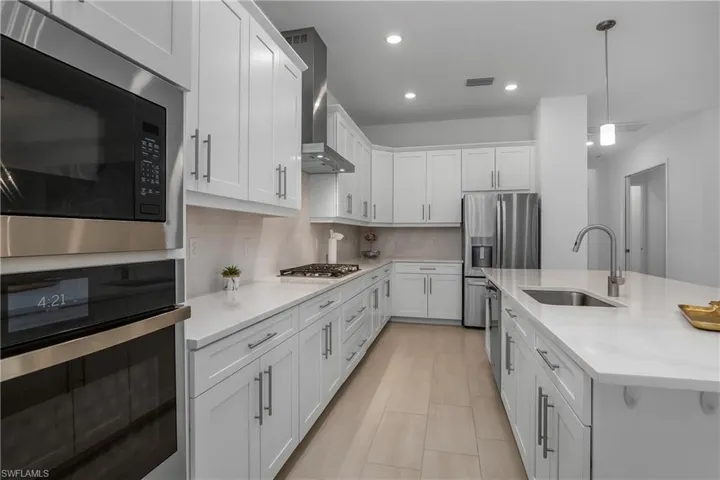 Kitchen with stainless steel appliances, a sink, recessed lighting, white cabinets, and wall chimney range hood