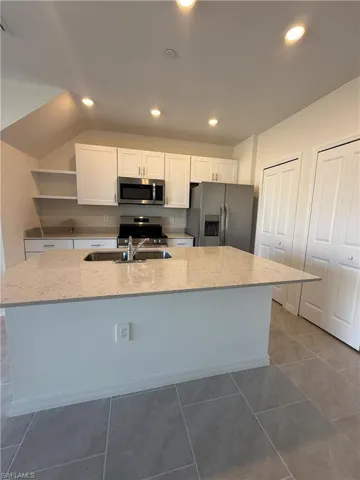Kitchen with white cabinetry, light stone counters, stainless steel appliances, a kitchen island with sink, and recessed lighting