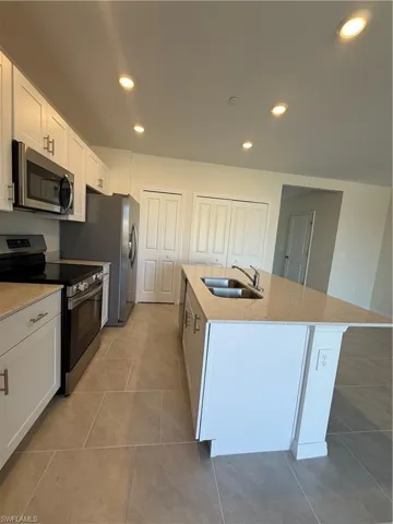 Kitchen featuring range, an island with sink, recessed lighting, white cabinetry, and light stone counters