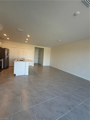 Kitchen featuring a kitchen island with sink, white cabinets, recessed lighting, open floor plan, and refrigerator