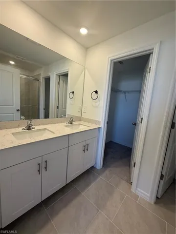 Full bathroom featuring double vanity, a spacious closet, a shower stall, and light tile patterned floors