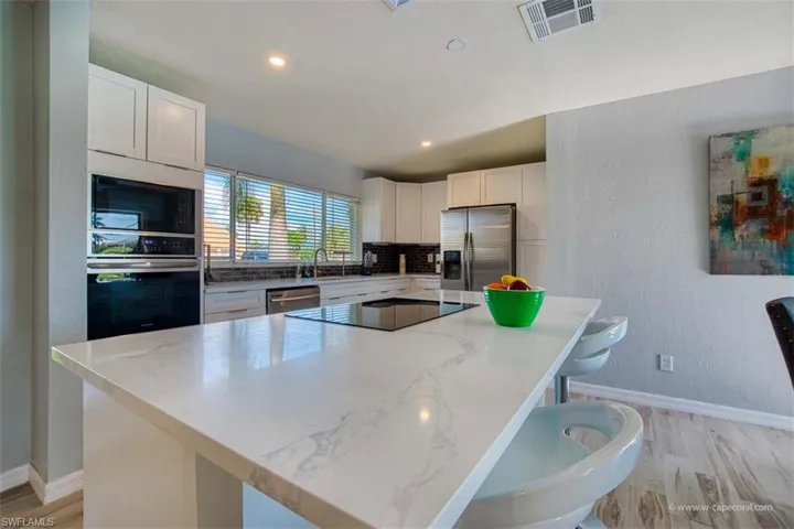Kitchen with white cabinets, a center island, a textured wall, black appliances, and light stone countertops