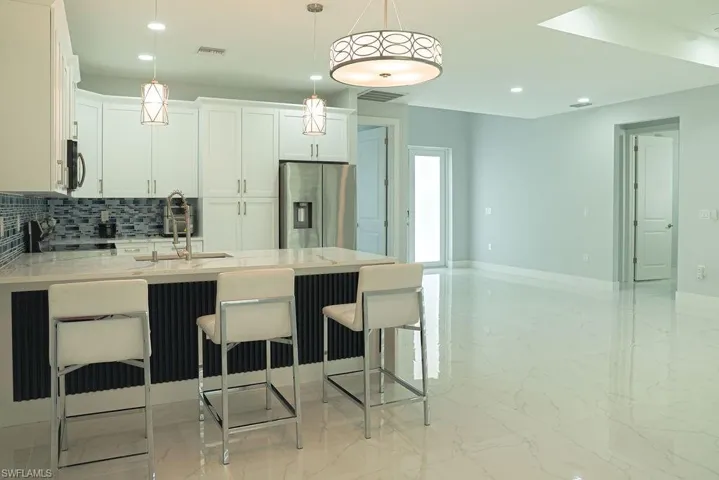 Kitchen featuring light marble finish floors, tasteful backsplash, stainless steel fridge, recessed lighting, and a peninsula