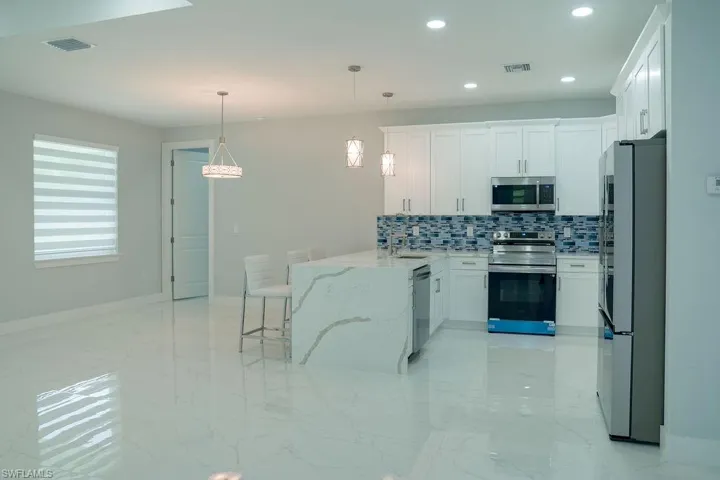 Kitchen with appliances with stainless steel finishes, light marble finish flooring, decorative backsplash, a peninsula, and white cabinets