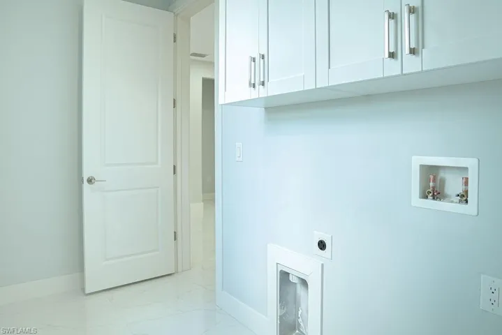 Washroom featuring electric dryer hookup, cabinet space, washer hookup, and light marble finish flooring