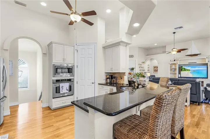 Kitchen featuring arched walkways, ceiling fan, dark stone counters, a peninsula, and a kitchen bar