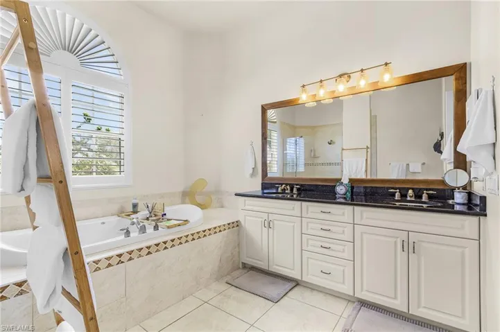 Bathroom featuring a garden tub, double vanity, light tile patterned floors, and a tile shower