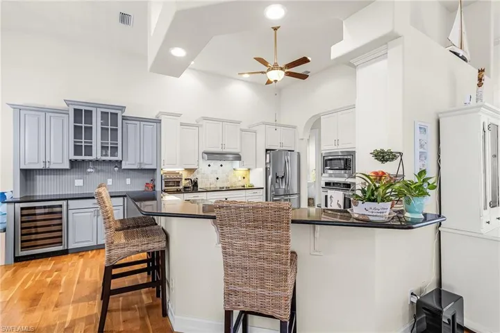 Kitchen featuring a kitchen bar, stainless steel appliances, beverage cooler, arched walkways, and tasteful backsplash