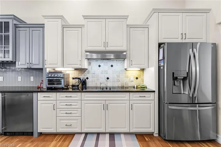 Kitchen with stainless steel fridge, dark stone countertops, and tasteful backsplash