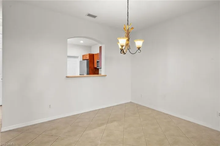 Empty room with a chandelier, light tile patterned floors, and arched walkways