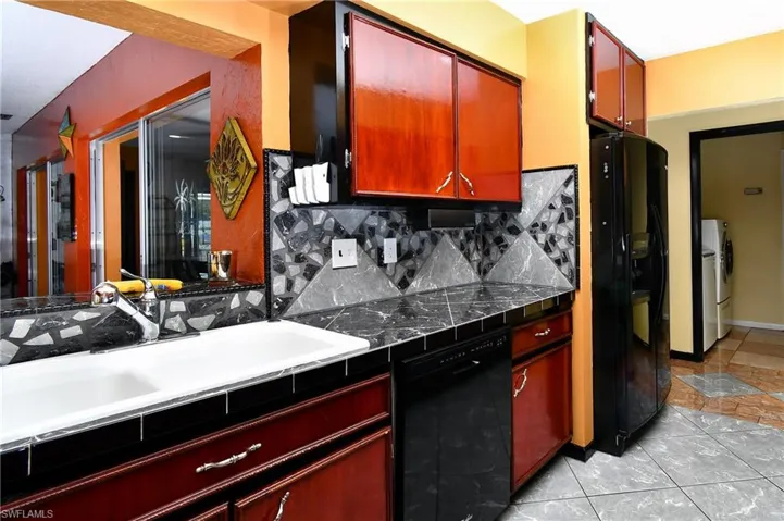Kitchen with sink, black appliances, washing machine and dryer, and decorative backsplash