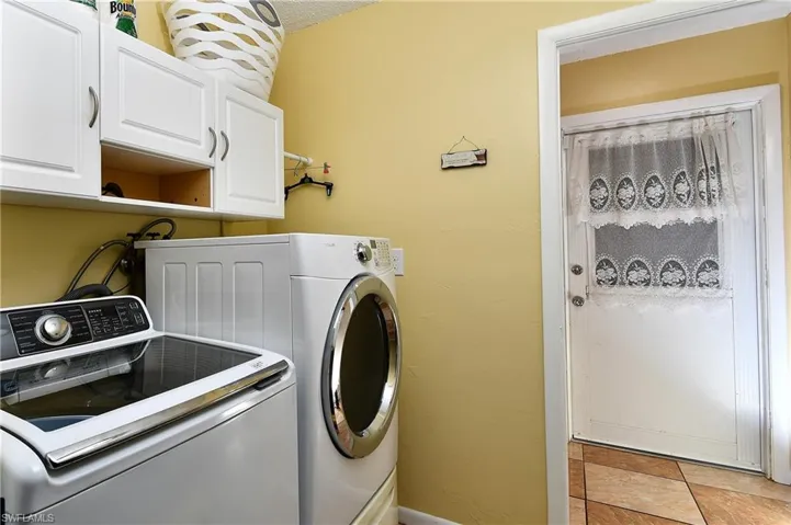 Washroom with washing machine and clothes dryer, light tile patterned floors, and cabinets