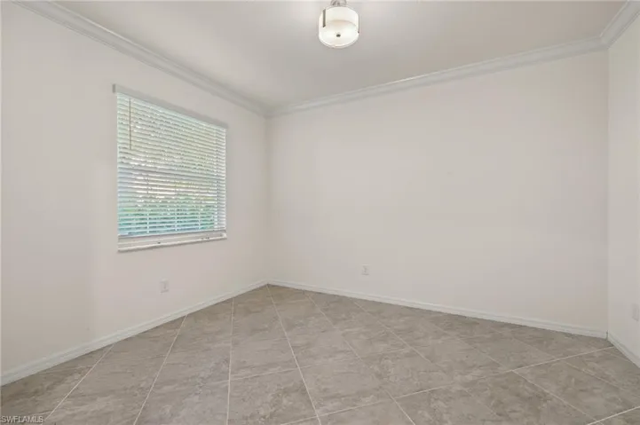 Tiled spare room featuring crown molding