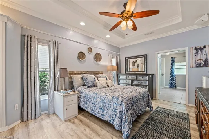Bedroom with ceiling fan, raised ceiling, light wood-type flooring, and ornamental molding