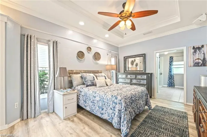 Bedroom with ceiling fan, light hardwood / wood-style flooring, ornamental molding, and a tray ceiling