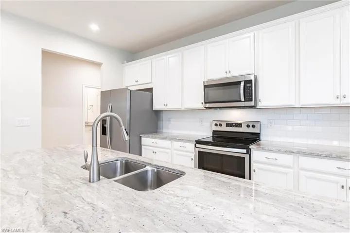 Kitchen featuring white cabinetry, sink, backsplash, light stone counters, and stainless steel appliances