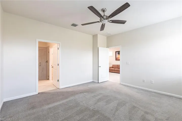 Unfurnished bedroom with ensuite bathroom, light colored carpet, and ceiling fan