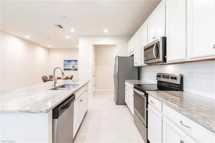 Kitchen featuring sink, stainless steel appliances, white cabinets, and a center island with sink