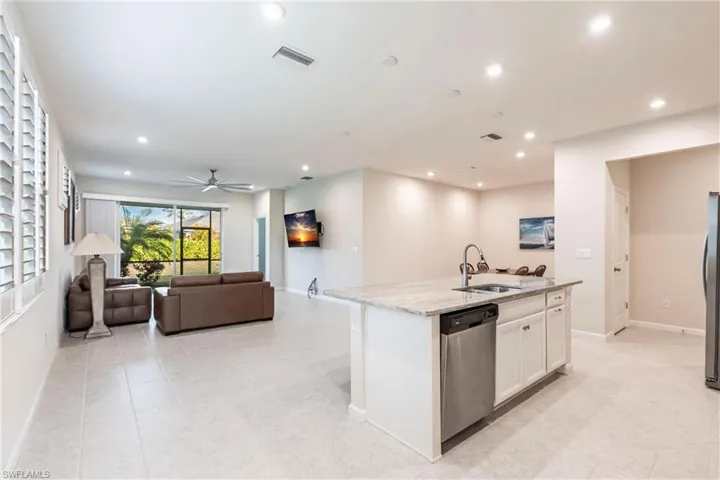 Kitchen with appliances with stainless steel finishes, an island with sink, sink, white cabinets, and light stone counters