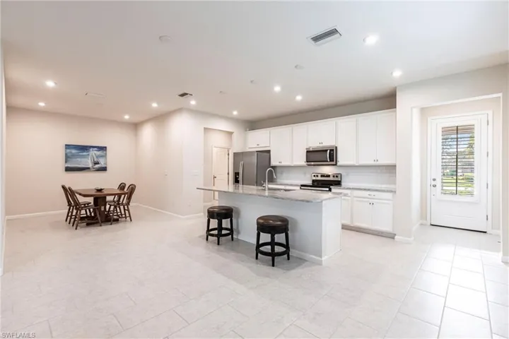 Kitchen featuring sink, a breakfast bar area, appliances with stainless steel finishes, a kitchen island with sink, and white cabinets