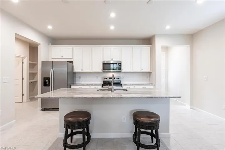 Kitchen featuring white cabinetry, appliances with stainless steel finishes, a kitchen island with sink, and light stone counters
