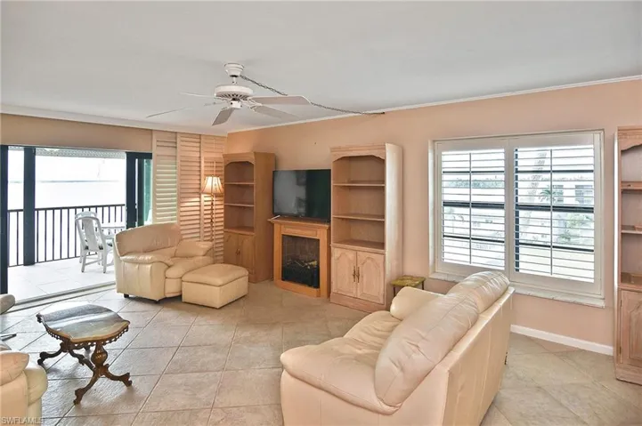 Living area with a fireplace, a ceiling fan, light tile patterned flooring, and crown molding