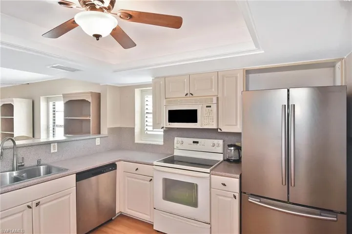 Kitchen with stainless steel appliances, a raised ceiling, light wood-style floors, a ceiling fan, and light countertops