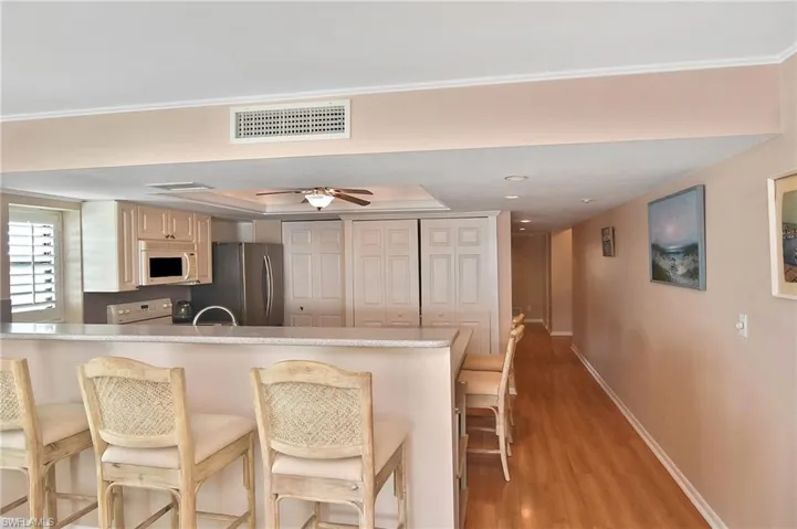 Kitchen with white appliances, light wood finished floors, a breakfast bar area, a peninsula, and a ceiling fan