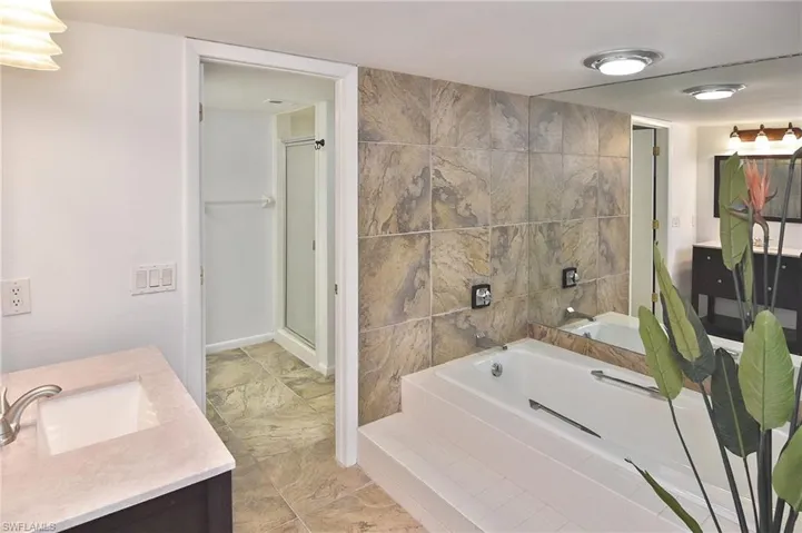 Bathroom featuring vanity, a garden tub, a stall shower, and tile walls