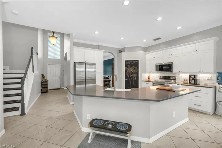 Kitchen featuring light tile patterned floors, tasteful backsplash, stainless steel appliances, white cabinets, and arched walkways