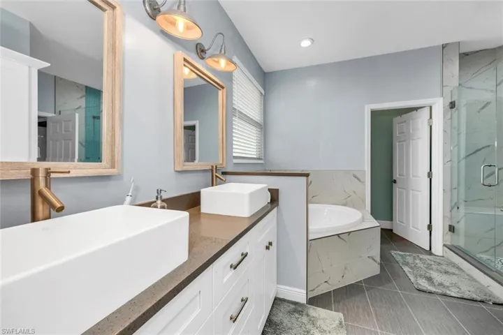Full bath with a bath, a marble finish shower, double vanity, dark tile patterned floors, and recessed lighting