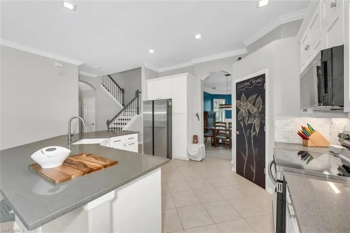 Kitchen featuring arched walkways, stainless steel appliances, dark stone counters, ornamental molding, and recessed lighting
