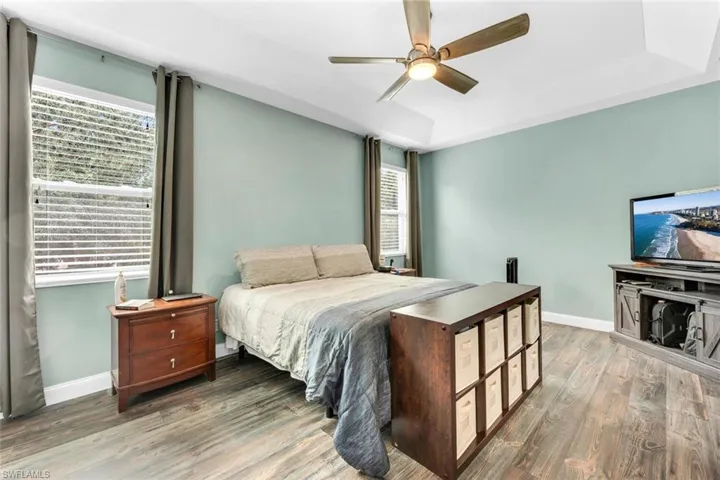 Bedroom featuring a raised ceiling, wood finished floors, and a ceiling fan