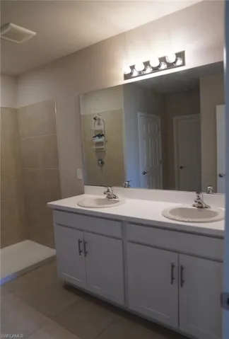 Full bath featuring double vanity, light tile patterned floors, and a tile shower