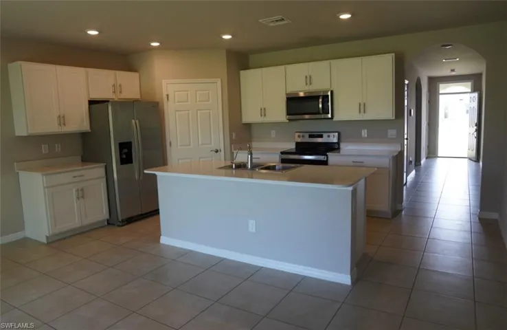 Kitchen featuring arched walkways, stainless steel appliances, light countertops, recessed lighting, and white cabinets